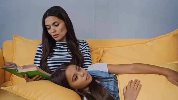 Mother reading aloud to daughter lying on pillow in living room — Stock Photo