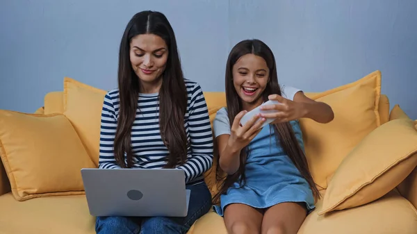 Glückliches Kind spielt Spiel auf Smartphone, während Mutter Laptop benutzt — Stockfoto