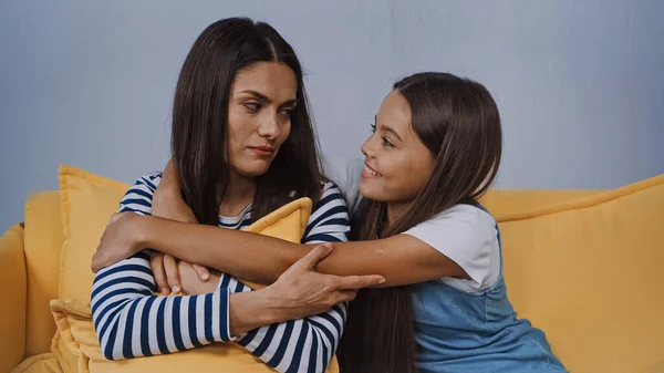 Smiling girl hugging upset mother in living room — Stock Photo