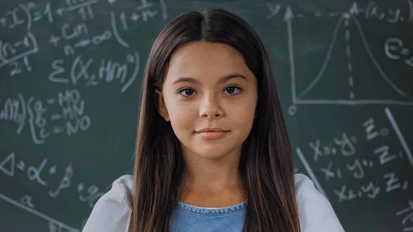 Joyful schoolkid looking at camera near chalkboard — Stock Photo