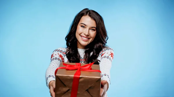 Femme souriante en pull tenant présent sur fond bleu — Photo de stock