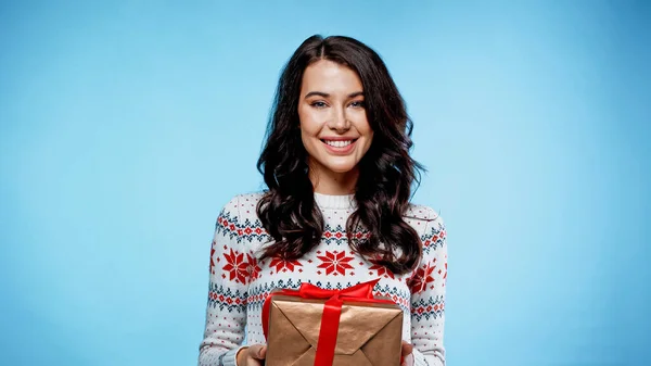Brünette Frau lächelt und hält Geschenk mit Schleife auf blauem Hintergrund — Stockfoto