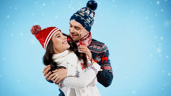 Весела пара в теплих капелюхах і светрах обіймається на синьому фоні — стокове фото