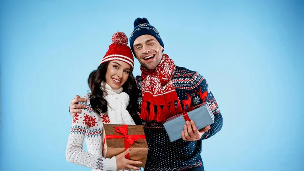 Smiling couple in warm sweaters holding gift boxes on blue background — Stock Photo