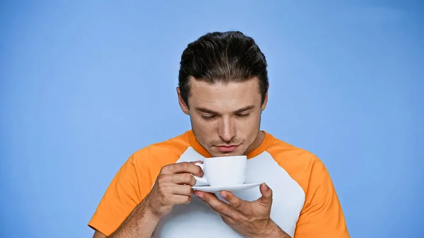 Hombre complacido con los ojos cerrados disfrutando del sabor del café aislado en azul - foto de stock