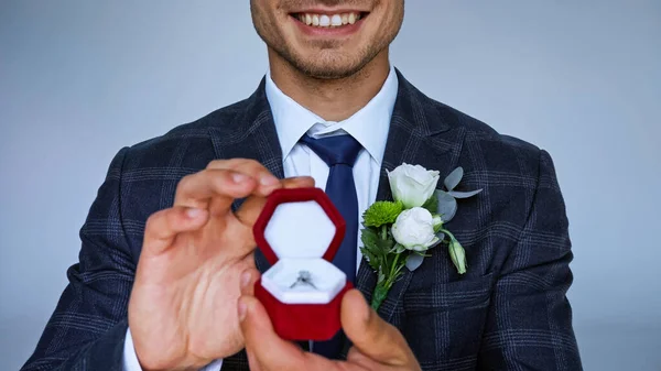 Vista cortada do noivo feliz mostrando caixa de jóias com anel de casamento em primeiro plano borrado isolado em azul — Fotografia de Stock