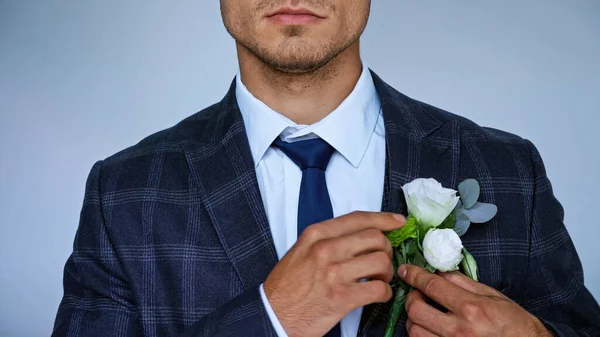 Partial view of elegant bridegroom fixing boutonniere isolated on blue — Stock Photo