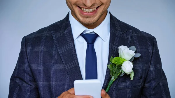 Vista recortada de novio feliz charlando en el teléfono inteligente aislado en azul - foto de stock