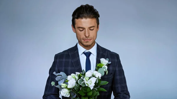Sconvolto sposo tenendo bouquet da sposa isolato su blu — Foto stock