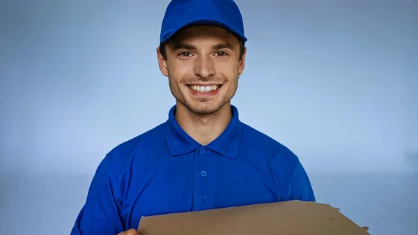 Cheerful delivery man with pizza box looking at camera isolated on blue — Stock Photo