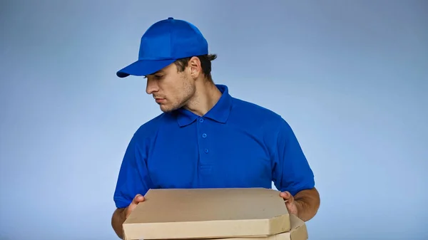 Zusteller schaut nach unten, während er Pizzakartons isoliert auf blauem Grund hält — Stockfoto