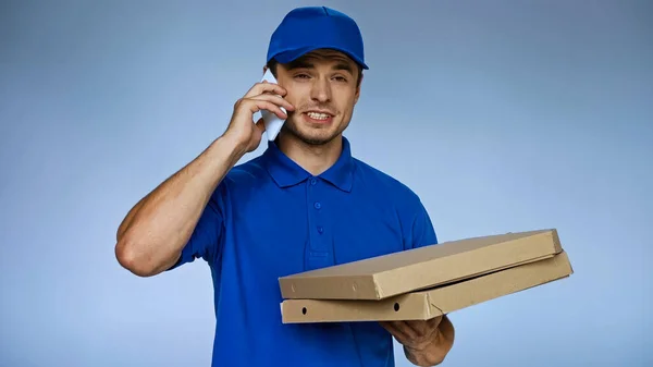 Skeptischer Zusteller spricht auf Smartphone und hält Pizzakartons isoliert auf blauem Grund — Stockfoto