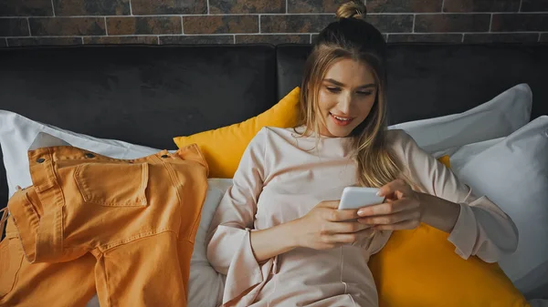 Mujer feliz joven mensajes de texto en el teléfono inteligente en la habitación de hotel - foto de stock