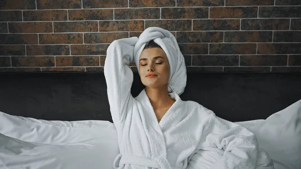 Femme avec les yeux fermés en serviette blanche reposant sur le lit dans la chambre d'hôtel — Photo de stock