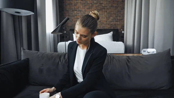 Mujer de negocios en ropa formal sentado en el sofá y mirando a la taza - foto de stock