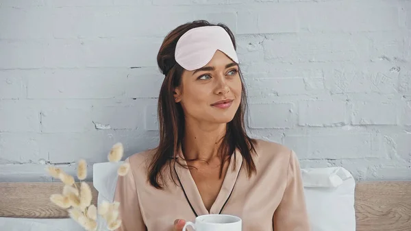 Joyful woman holding cup of coffee and looking away in bedroom — Stock Photo