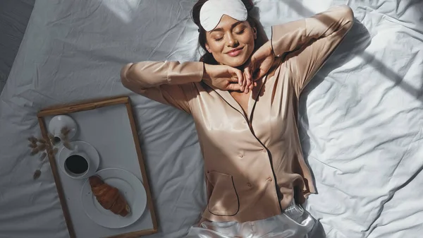 Вид зверху щасливої жінки, що розтягується в ліжку біля лотка зі смачним сніданком — стокове фото