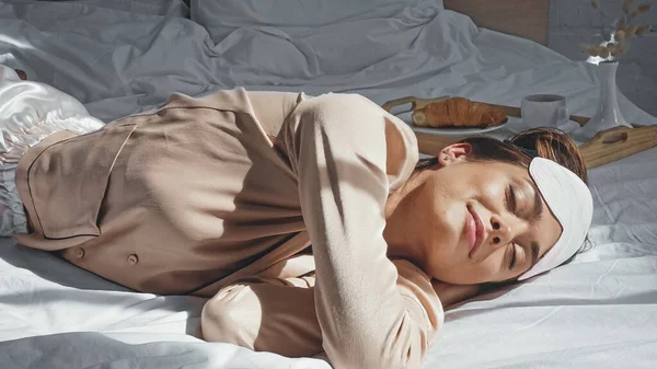 Mulher satisfeita com os olhos fechados deitado na cama perto da bandeja com café da manhã — Fotografia de Stock