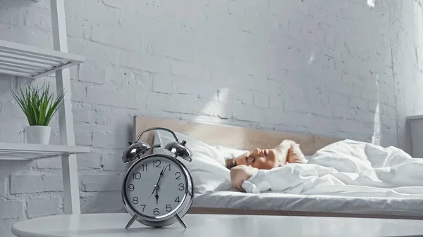 Despertador retro cerca de la mujer somnolienta acostada en la cama por la mañana - foto de stock
