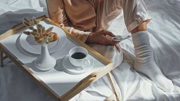 Cropped view of woman using smartphone near tray with tasty breakfast — Stock Photo