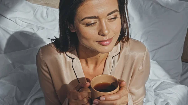 Vue grand angle de femme heureuse tenant tasse de thé et regardant loin — Photo de stock