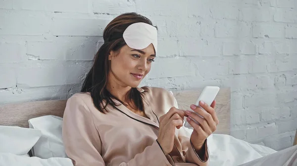 Mulher feliz em mensagens de texto máscara olho no smartphone no quarto — Stock Photo