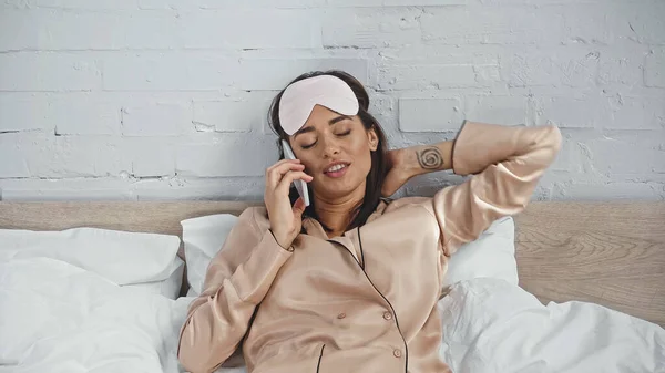 Tätowierte Frau mit Augenmaske spricht im Schlafzimmer auf Smartphone — Stockfoto