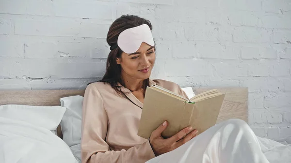 Felice donna in maschera occhi lettura libro a letto — Foto stock