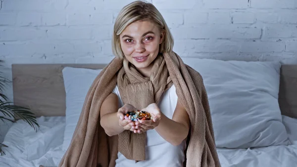 Donna malata con una manciata di pillole sorridenti alla macchina fotografica in camera da letto — Foto stock
