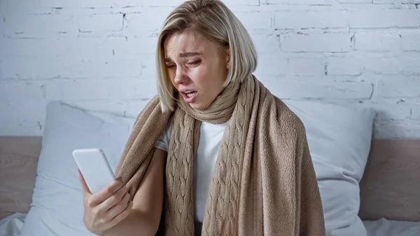 Sick, displeased woman looking at mobile phone in bedroom — Foto stock