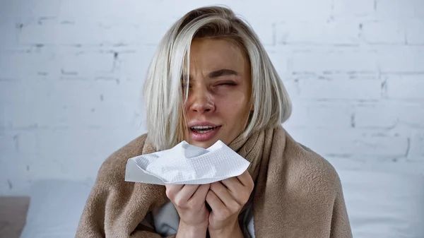 Sick woman holding paper napkin while sneezing in bedroom — Stock Photo