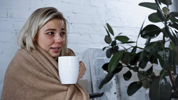 Sick woman holding cup of tea while watching movie in bedroom — Stock Photo