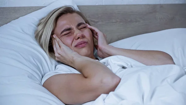 Больная женщина, касающаяся головы, страдающая головной болью в постели — стоковое фото