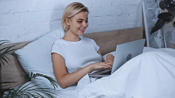 Blogueiro alegre digitando no laptop no quarto — Fotografia de Stock