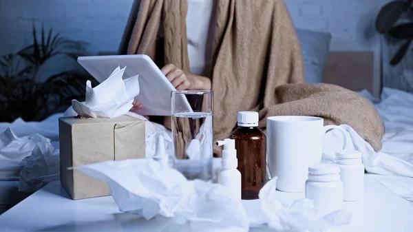 Cropped view of sick woman using digital tablet near medications, drinks and paper napkins on blurred foreground — Stock Photo