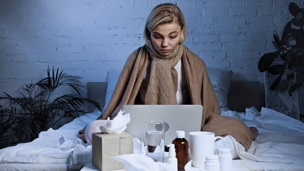 Ill freelancer working on laptop under blanket in bedroom — Stock Photo