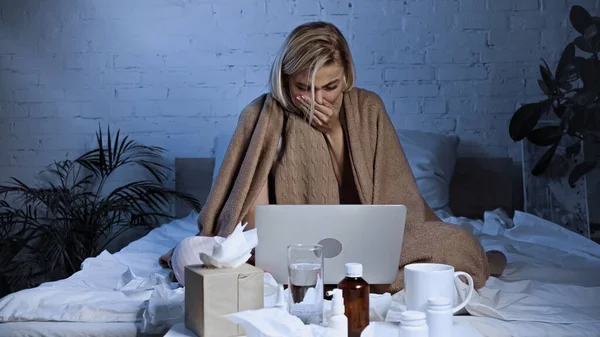 Diseased freelancer sneezing near laptop and medications in bedroom — Stock Photo