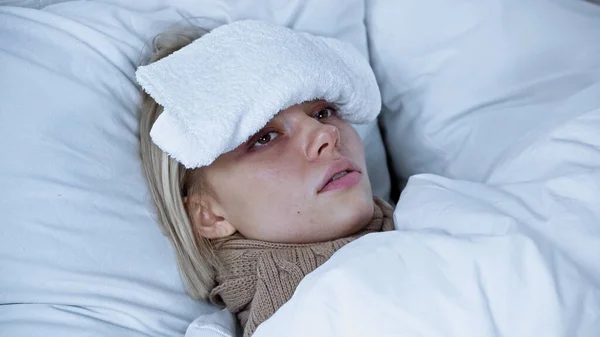 Young diseased woman lying in bed with compress on forehead — Stock Photo