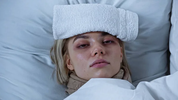 Sick young woman lying in bed with towel on forehead — Stock Photo