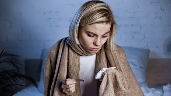 Mujer joven enferma sosteniendo pastillas y leyendo medicamentos recetados - foto de stock