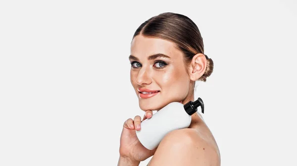 Mujer joven sosteniendo botella cosmética y posando aislado en blanco - foto de stock