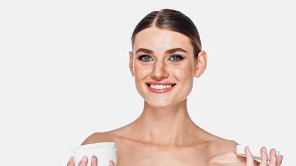 Mujer feliz sosteniendo frasco con crema cosmética aislado en blanco - foto de stock