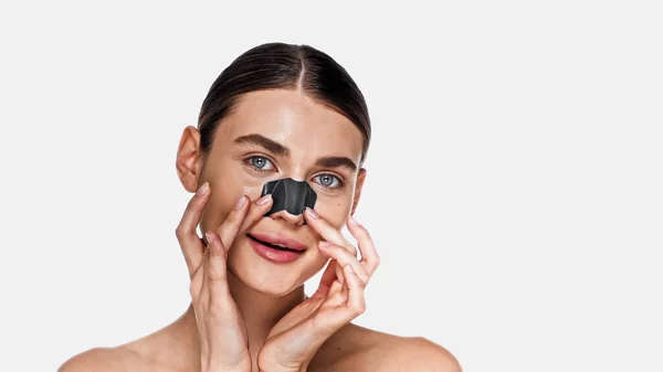 Femme adulte souriante appliquant une tache de point noir sur le nez isolé sur blanc — Photo de stock