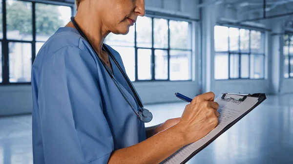 Обрізаний вид зрілого лікаря, що пише на кишені в лікарні — стокове фото