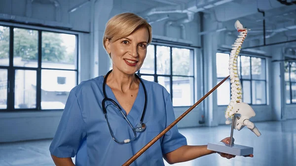 Médecin souriant avec pointeur tenant modèle de colonne vertébrale en clinique — Photo de stock