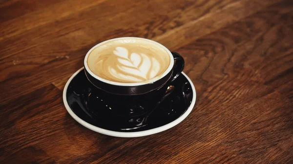 Taza de delicioso capuchino con latte arte en la mesa - foto de stock