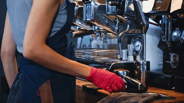 Vista ritagliata di barista vicino portafilter con caffè macinato in caffetteria — Foto stock