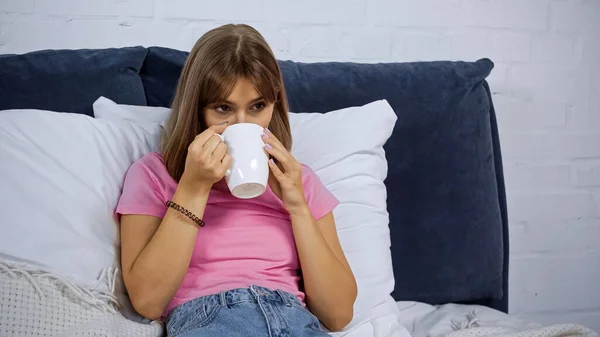 Молодая женщина пьет кофе и во время просмотра фильма в спальне — стоковое фото