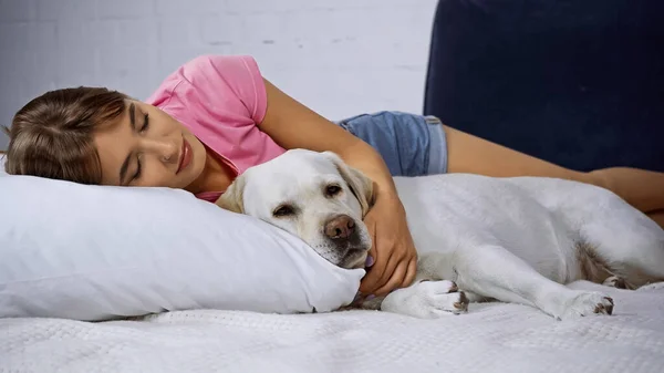 Jeune femme avec les yeux fermés couché avec golden retriever sur le lit — Photo de stock