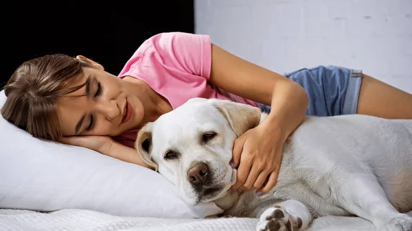 Junge Frau liegt auf Bett und kuschelt Golden Retriever — Stockfoto